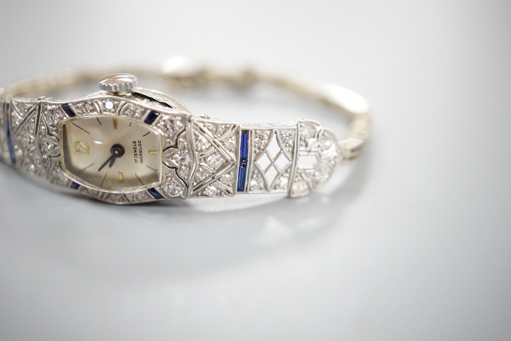 A lady's mid 20th century white metal, sapphire and diamond cluster set cocktail watch, on a 9ct bracelet (a.f.), gross weight 17.2 grams.